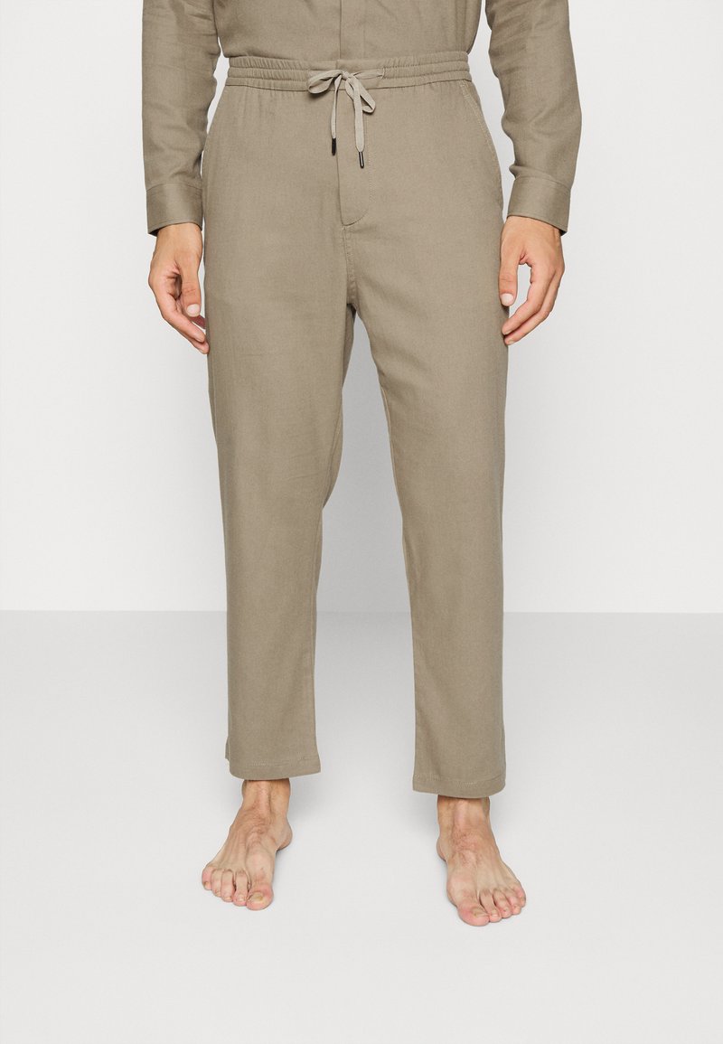 Calças de linho bege com cintura elástica, cordão, comprimento até ao tornozelo e textura suave. Sem padrões ou detalhes adicionais visíveis.