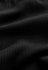 Schwarzer gerippter Stoff mit sichtbarer vertikaler Strickstruktur, der weiche Falten und Schatten zeigt, die eine wellige Oberfläche erzeugen.