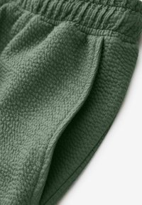 Pantaloni corte verdi in tessuto con superficie testurizzata e intrecciata, dotati di una vita elastica e pieghe laterali per una maggiore struttura e comfort.