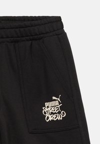 Μαύρη τσέπη σε φόρμα από φούτερ με ελαστική μέση και λευκό λογότυπο "Puma Street Crew" και σιλουέτα του puma τυπωμένα στο ύφασμα.