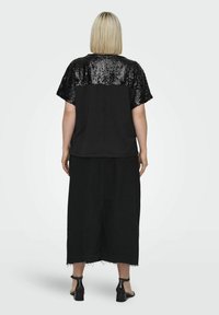 Czarna bluzka z krótkimi rękawami ozdobionymi cekinami, w połączeniu z czarną spódnicą do kolan z postrzępionym wykończeniem i butami wsuwanymi.