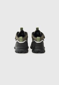 Chaussures de sport avec une semelle en caoutchouc noir, un dessus en textile vert, un renfort au talon et une sangle ajustable. Comprend des languettes de tirage au talon.