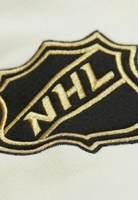 Gesticktes NHL-Logo in Schwarz und Gold auf einem cremefarbenen Stoffhintergrund, mit einer schildförmigen Form und aufwendigen Stickdetails.