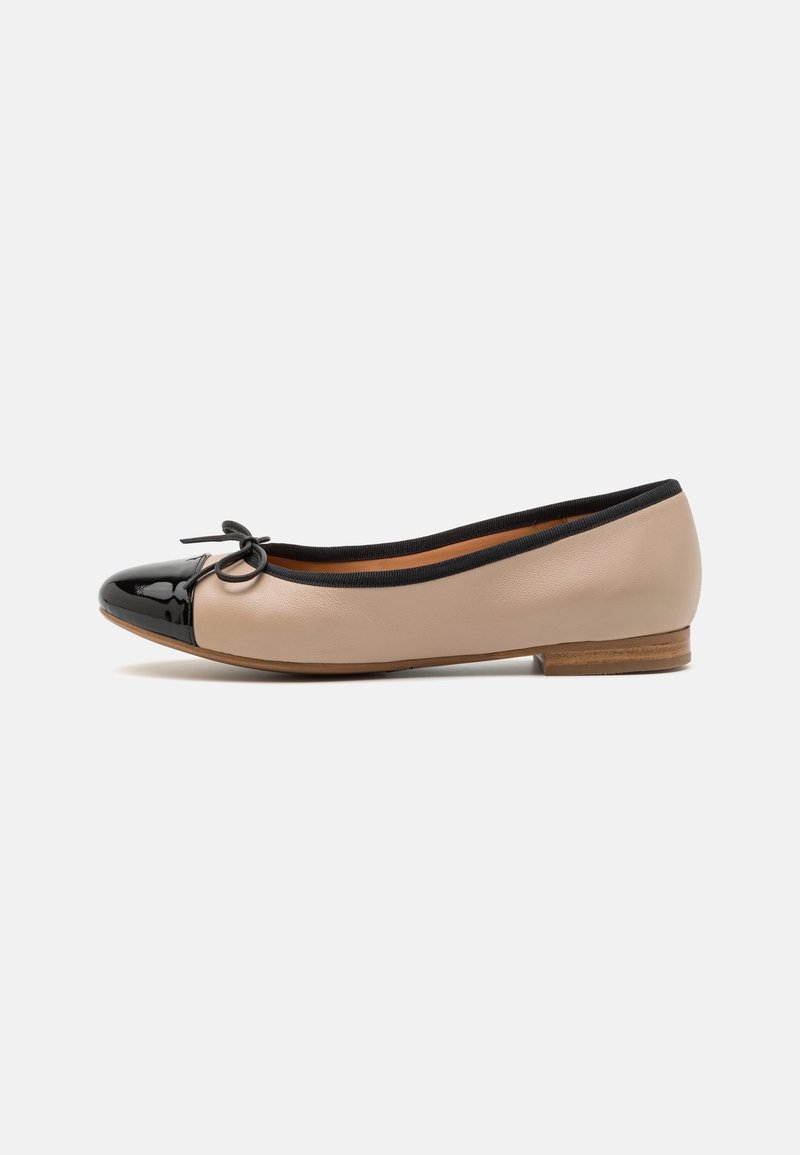 Chaussure ballerine beige avec embout verni noir, bordure noire, petit nœud sur le dessus et talon en bois bas sur fond blanc.