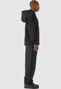 Felpa nera con tasca a marsupio e cappuccio regolabile, abbinata a pantaloni cargo in denim scuro con tasche laterali e tessuto texturizzato. Sneakers nere.