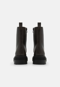 Bottines en cuir lisse marron foncé avec une semelle noire robuste, dotées d'une fermeture éclair et de languettes à l'arrière pour un enfilage facile.