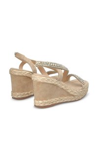 Sandales compensées en daim beige avec une semelle en jute tissée. Elles présentent deux brides scintillantes ornées de strass pour un détail supplémentaire.