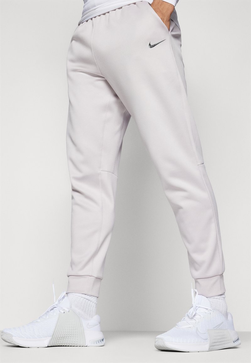 Des joggings Nike gris clair présentent un design fuselé, une ceinture élastique et des poches latérales. Associés à des baskets Nike blanches.