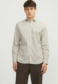 Camisa de manga larga con botones, que presenta una base crema con un patrón geométrico en colores suaves. Tejido suave, cuello clásico y corte ajustado.
