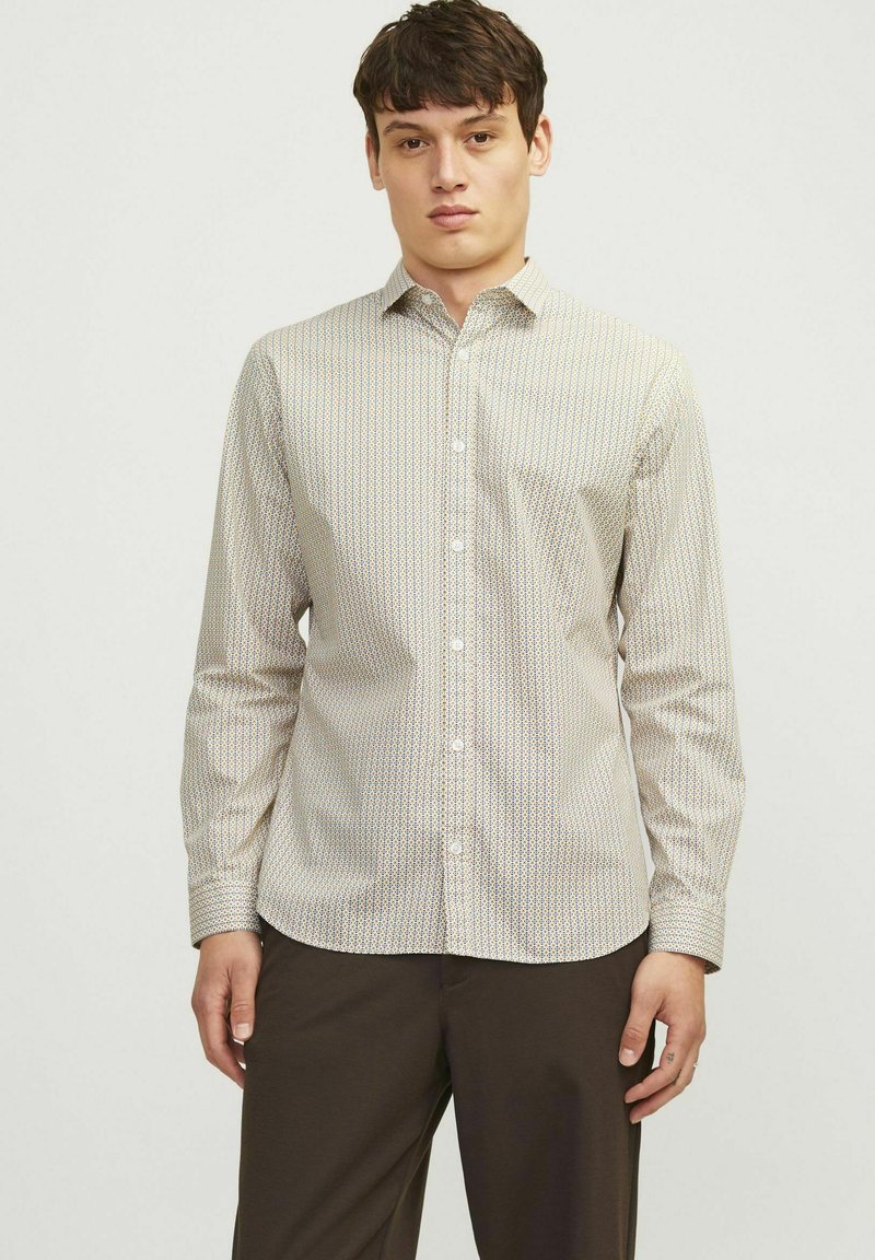 Camisa de manga larga con botones, que presenta una base crema con un patrón geométrico en colores suaves. Tejido suave, cuello clásico y corte ajustado.