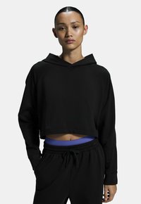 Fekete, kapucnis, rövid fazonú pulóver, hosszú ujjakkal, laza szabással. Sima anyag ribbelt részletekkel. Fekete melegítőnadrággal párosítva.