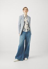 Lichtblauwe blazer over een crèmekleurig overhemd met polka dots, gecombineerd met wijduitlopende blauwe denim jeans en witte sneakers. Eenvoudig en modern ontwerp.