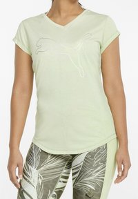 Ljusgrön idrottströja med v-ringning och korta ärmar. Har en silverfärgad Puma-logotyp. Tyget är mjukt med en något texturerad yta.