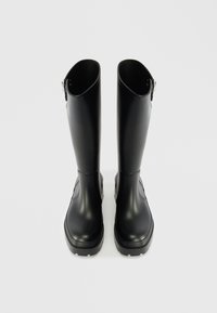 Bottes de pluie en caoutchouc noir avec une finition lisse, un design haut et une semelle texturée. Présente une fermeture éclair sur le côté et un bout arrondi.