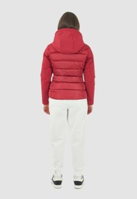 Giacca a vento rossa con cappuccio, caratterizzata da un design trapuntato e polsini elasticizzati. Indossata con pantaloni della tuta bianchi e sneaker nere.