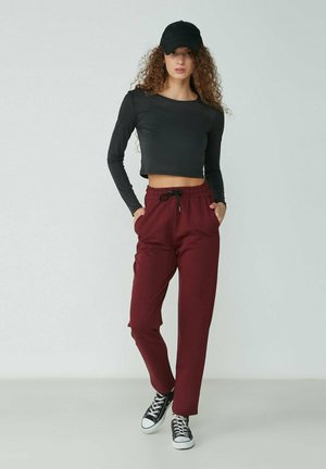Black long-sleeve cropped top paired with burgundy elastic waistband pants. Pants feature side pockets. Black cap and sneakers complete the look.