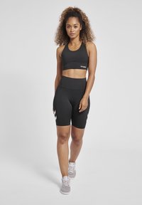 Svart sportbh och högmidjade shorts med vit chevron-design. Modellen bär grå sneakers. Slät, stretchig tyg, figurnära design.