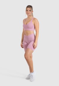 Sujetador deportivo rosa y pantalones cortos de tiro alto a juego, hechos de tejido elástico. Presenta una textura suave y costuras mínimas. Zapatillas blancas.