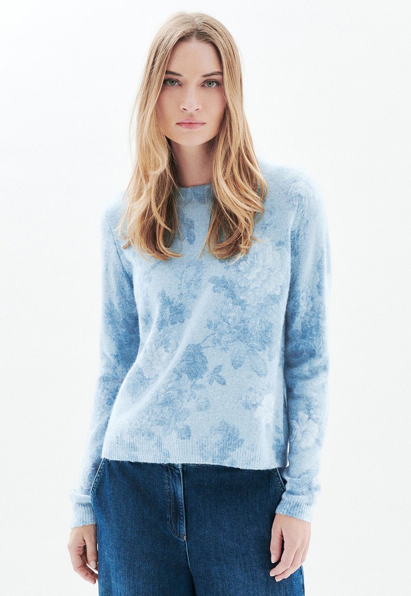 Jasnoniebieski sweter z kwiatowym wzorem, długimi rękawami, okrągłym dekoltem i miękką fakturą, zestawiony z ciemnoniebieskimi dżinsami.
