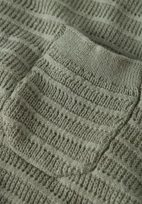 Gestrickter Pullover in gedämpftem Grün mit strukturierten Streifen und einer aufgesetzten Tasche. Das Material wirkt weich und leicht, mit einem gerippten Ausschnitt.