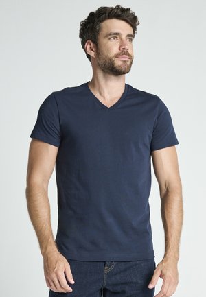 Camiseta de algodón azul marino con diseño de cuello en V, mangas cortas y textura lisa, llevada por un hombre frente a un fondo neutro.
