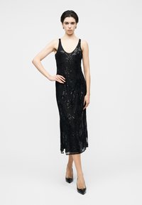 Sort blondekjole med en tætsiddende pasform, V-udskæring og indviklede blomsterapplikationer med palietter, der når til midt på læggen. Kombineret med spidse hæle.