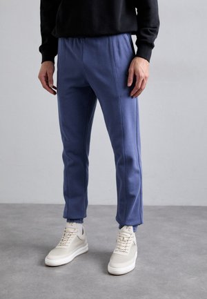 Blå sweatpants med en strækbar talje og sidesømme, parret med beige sneakers. Stoffet ser blødt ud med en afslappet pasform.