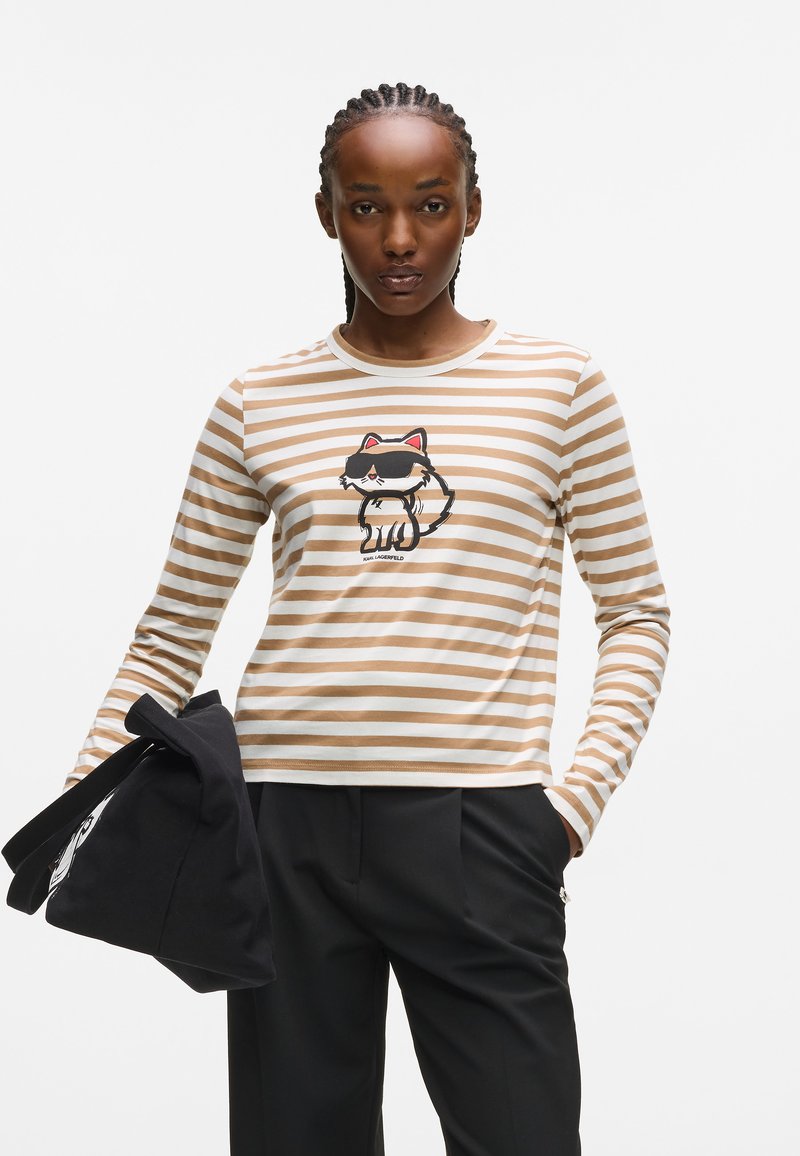 Randig långärmad skjorta i beige och vitt med en kattillustration framtill. Matchas med skräddarsydda svarta byxor och en svart väska.