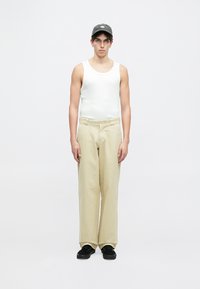 Hvit singlet, beige vide bukser, svarte sko og en mørk caps. Enkel design, lett stoff og nøytrale farger. Forfra.