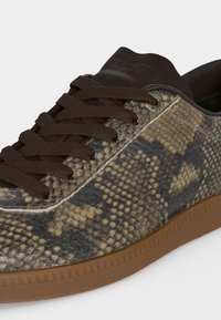 Gros plan d'une basket avec des lacets marron, une tige en cuir imprimé serpent, une languette brun foncé et une semelle en gomme.