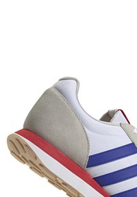 Sneaker z białą siateczkową cholewką, szarym zamszowym akcentem, czerwoną gumową podeszwą i niebieskimi poziomymi paskami po bokach. Niskoprofilowy design.