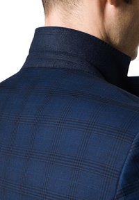 Granatowa marynarka w kratę charakująca się fakturowanym kołnierzem, wyraźnymi ramionami i szczegółowym przeszyciem, podkreślająca nowoczesny, dopasowany design.