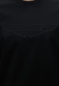 Μαύρο ύφασμα με κεντημένο λογότυπο Aston Martin με φτερά και το όνομα της μάρκας στο κέντρο.