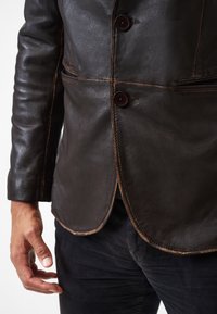 Braune Lederjacke mit glatter Textur, ausgestattet mit zwei Knöpfen, einem dezenten Glanz und kontrastierenden Nähten entlang der Ränder.