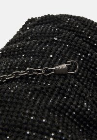 Musta clutch-laukku, jossa on tekstuuripinta pienistä pyöreistä helmistä, hopeaketju ja -kiinnitys.