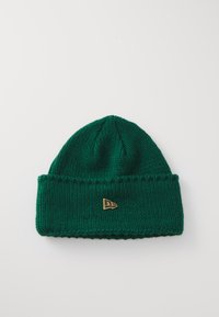 Căciulă tricotată verde cu manșetă ribbed, având un mic accent de logo auriu. Textura este moale și groasă, potrivită pentru vreme rece.