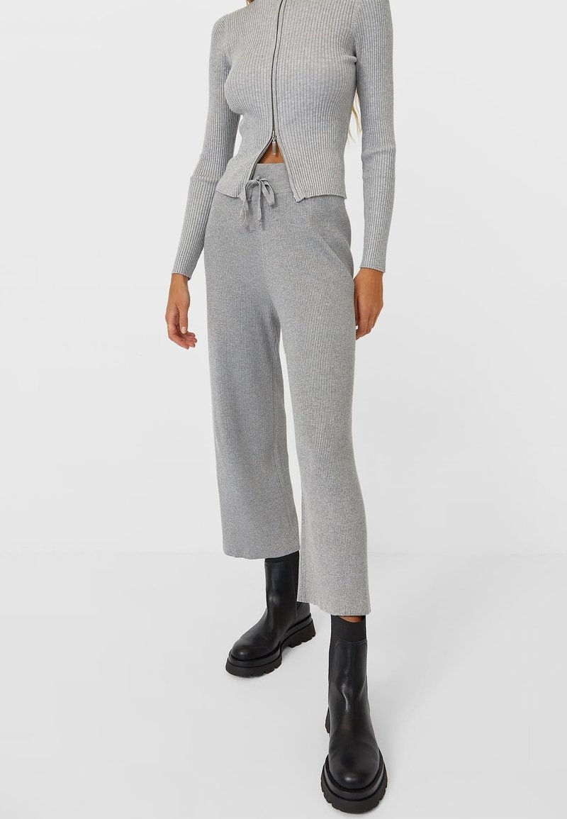 Pull gris côtelé zipé ajusté et pantalon en maille larges assortis, associés à des bottines noires à plateforme épaisses.