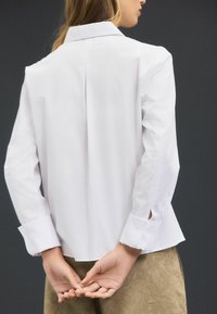 Witte blouse met kraag, lange mouwen met uitsparingen en een rugvouw; gladde textuur en op maat gemaakte ontwerp.