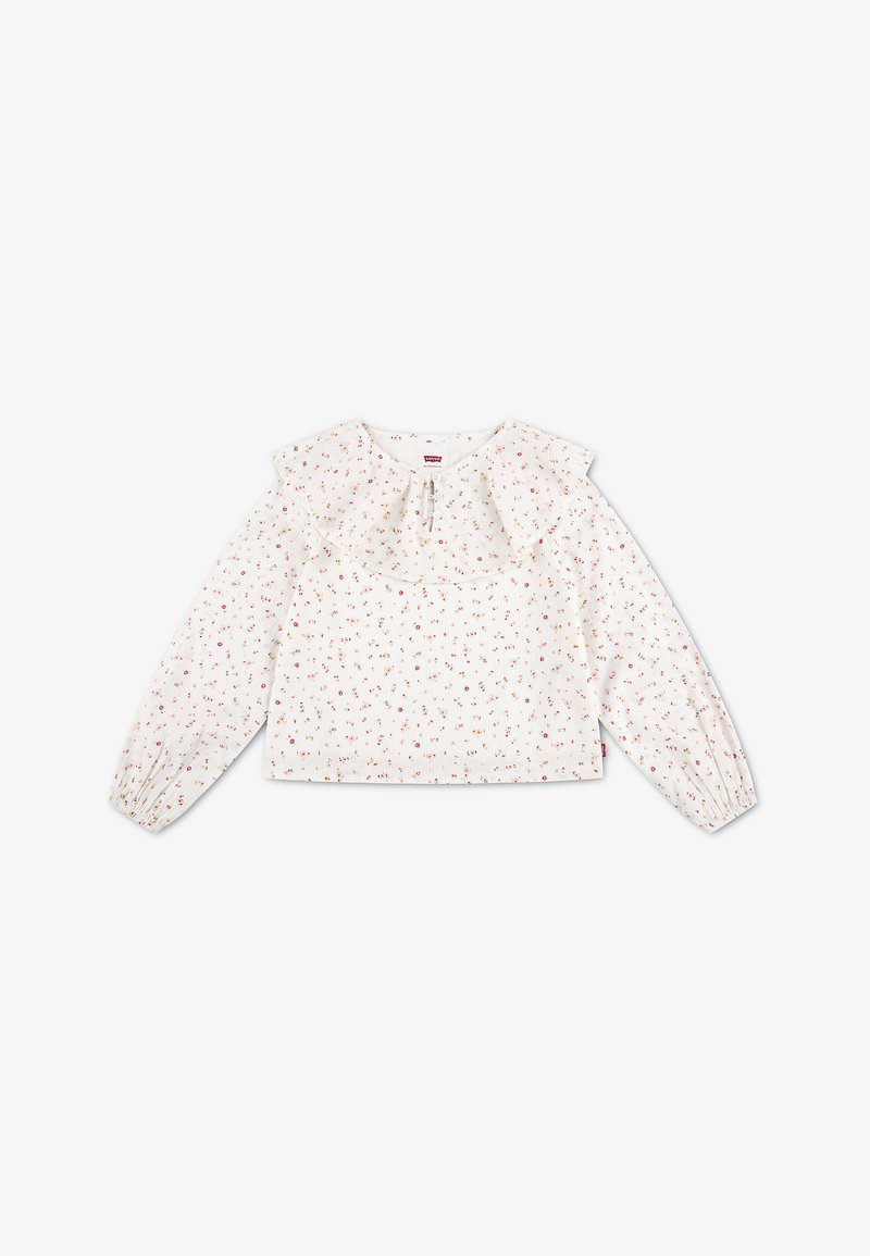 Blouse blanche à manches longues avec petit imprimé floral rouge, col volanté, encolure en forme de clé avec lien, et poignets élastiqués.