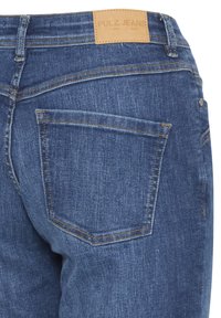 Donkerblauwe denim jeans met een leren label met "PULZ JEANS" op de tailleband, en één achterzak met zichtbare stiksels.