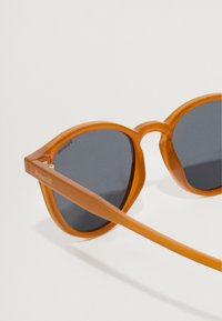 Πορτοκαλί διαφανή γυαλιά ηλίου με σκούρους φακούς, σε στρογγυλή γατίσια μορφή και λεία υφή. Λογότυπο "Polaroid" στη γέφυρα.