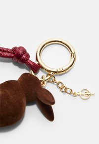 Brun velour kanin charm med en maroon fletning, fastgjort til en guldtonet metal nøglering og en kæde med en clasp detalje.