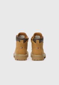 Bottines en cuir tan avec des accents marron, finition texturée et tirette à l'arrière. Présente un détail de logo et une semelle en caoutchouc avec un motif antidérapant.