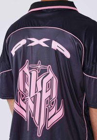 Maglietta sportiva nera con dettagli rosa. Presenta un grande testo grafico rosa sul retro e un colletto con finiture rosa a contrasto. Tessuto liscio e leggero.