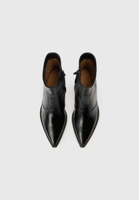 Čierne kožené členkové čižmy s špicatou špičkou, bočnými zipsami a hladkou textúrou. Vnútro vystlané hnedým materiálom.