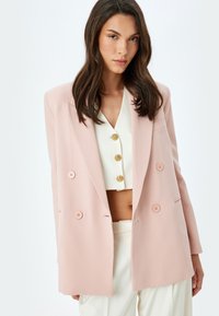 Hellrosa doppelreihige Blazerjacke mit Reverskragen, ausgestattet mit vier runden Knöpfen, seitlichen Taschen und einer glatten Stoffstruktur.