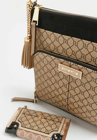 Borsa beige con texture a motivo, dettagli neri, hardware dorato e un pendente. Accanto c'è un portafoglio più piccolo con un design simile.