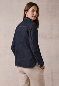 Camicia in denim scuro con colletto, polsini bottonati e fessure laterali, caratterizzata da dettagli di cucitura sottili e una vestibilità rilassata.