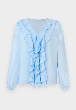 Ljusblå blus med V-ringning och volangdetalj fram. Långa ärmar med elastiska manschetter, och tyget verkar mjukt och lätt.