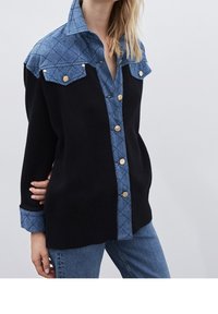 Svart stickad topp med en denimliknande, diamantmönstrad axel och krage, med guldknappar och ribbad nederkant.